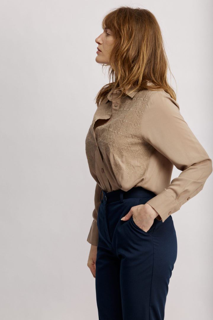 Janice מכופתרת בז' בגזרה קלאסית בעלת עיטורי רקמה עדינים בחזית. משכית