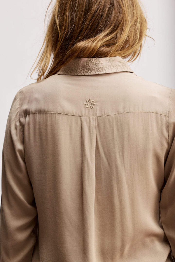 Janice מכופתרת בז' בגזרה קלאסית בעלת עיטורי רקמה עדינים בחזית. משכית